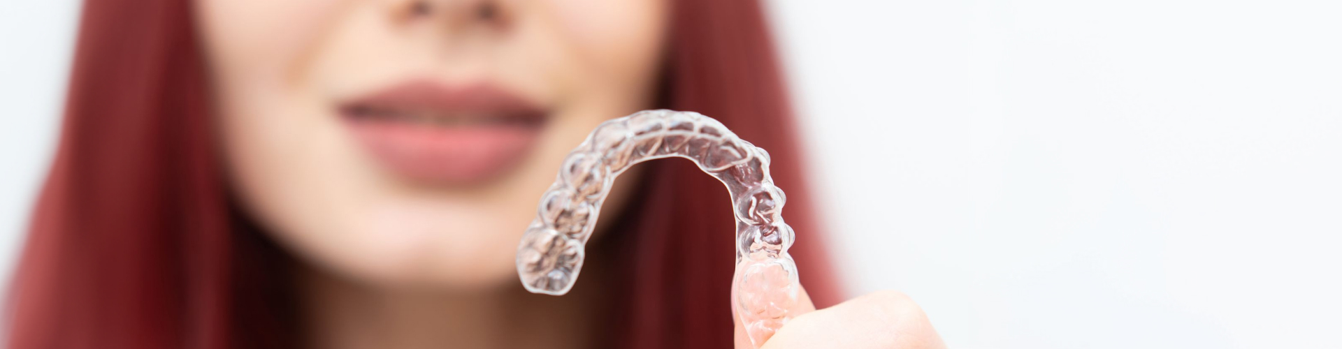 Person holding a clear aligner tray in the foreground, highlighting transparent orthodontic treatment for discreet teeth straightening.
